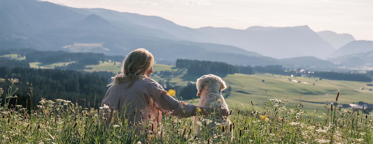 Katharina Miklauz mit Nala sitzen auf einer Wiese und schauen über die Landschaft