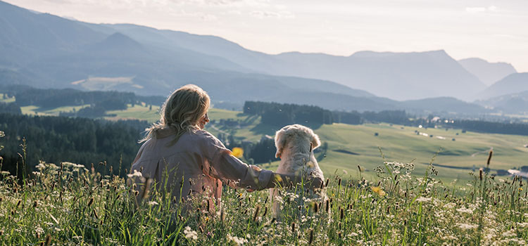 Katharina Miklauz mit Nala sitzen auf einer Wiese und schauen über die Landschaft