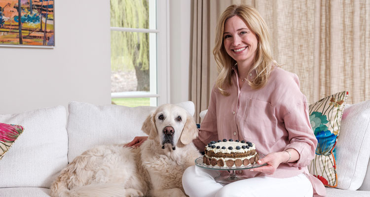 Katharina Miklauz sitzt mit Ihrer Hündin Nala auf der Bank und hält den gebackenen Kuchen in der Hand