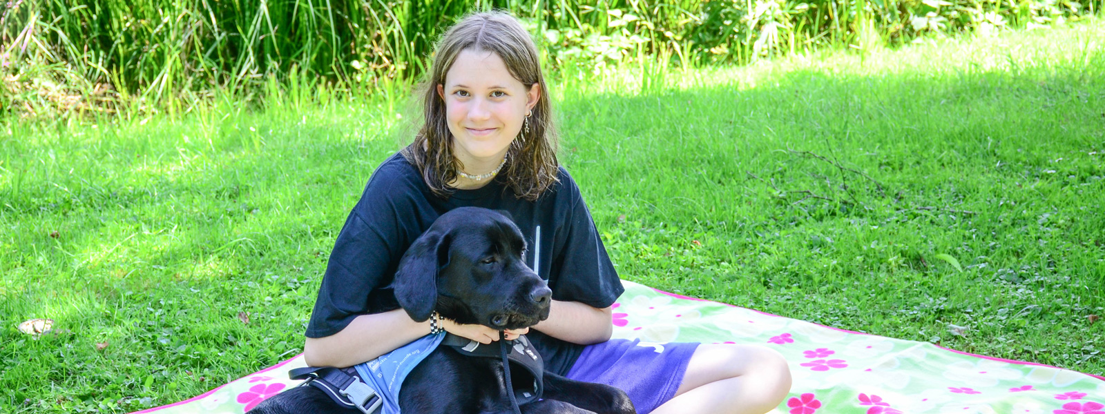 Nina wie sie mit ihrem Hund Ezra auf der Wiese sitzt